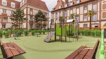 A playground with climbing structures and a slide, surrounded by benches and a green fence.