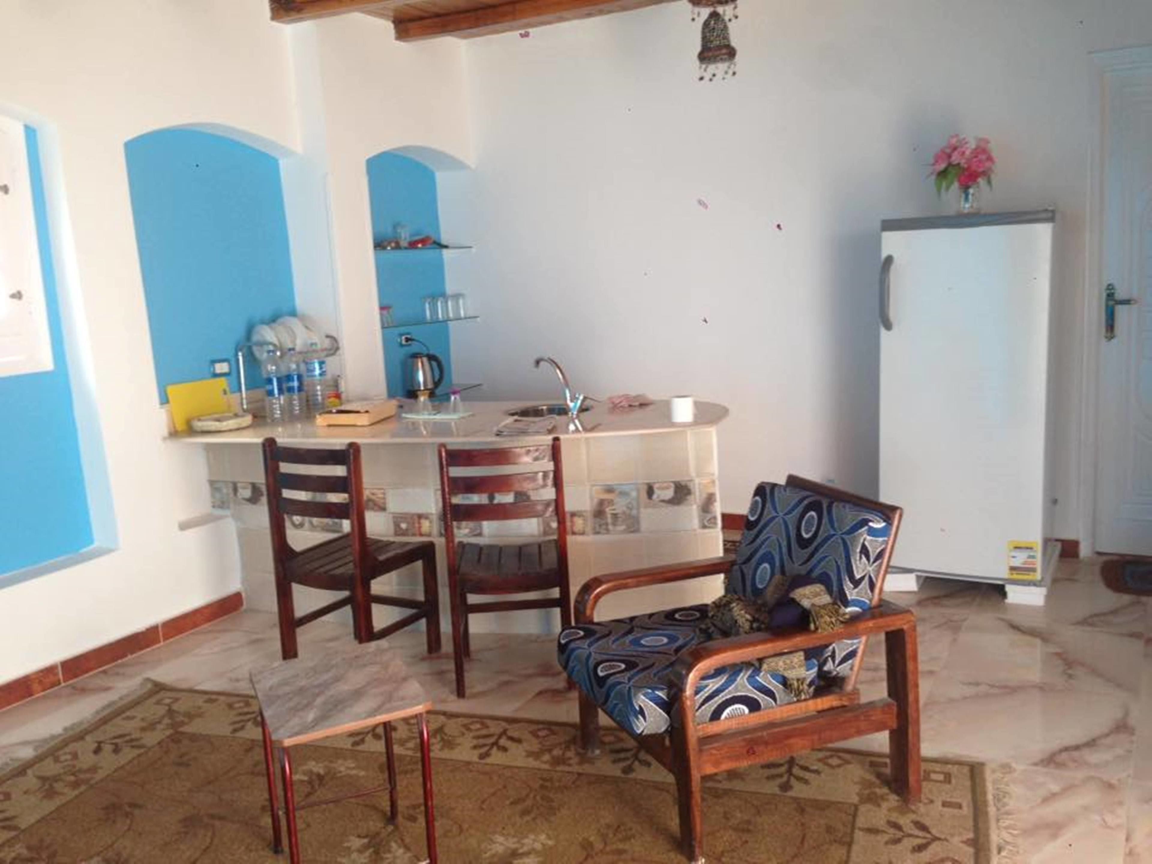 A compact kitchen with a dining area, featuring a small refrigerator, a sink, and a dining table with chairs.