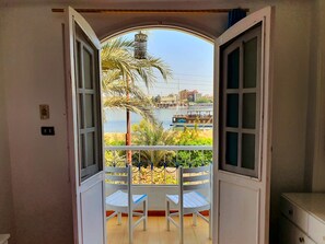 An open door leading to a balcony with a view of a body of water, boats, and buildings. - Luxor Guest House (Luxor)