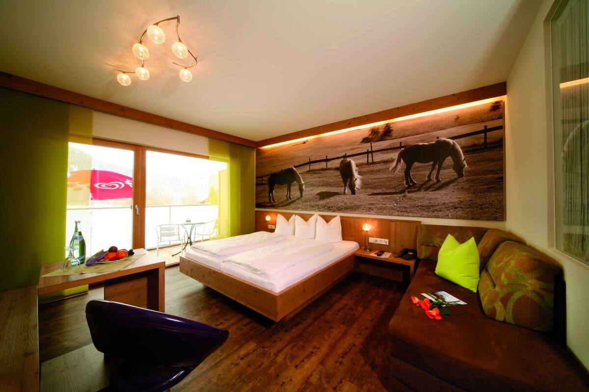 Un dormitorio con una cama, un escritorio de madera, una silla, un sofá y una obra de arte en la pared con caballos.