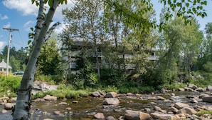 Un río con rocas, rodeado de árboles y un edificio con balcones.