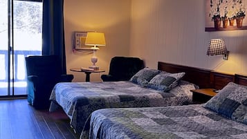 Habitación de hotel con dos camas, una silla, una mesita, una lámpara y un cuadro en la pared.