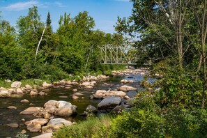 A river with large rocks, surrounded by dense green trees and a metal bridge in the background. - The Wayside Inn (Bethlehem)