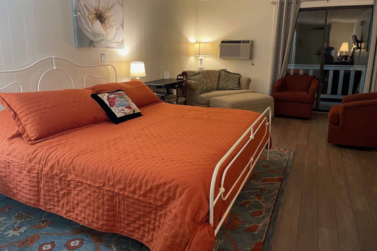 A hotel room with a large bed, a sofa, a chair, a table, and a painting on the wall.