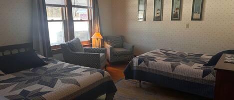 Une chambre d’hôtel avec deux lits, une chaise, une lampe et une fenêtre avec des rideaux.