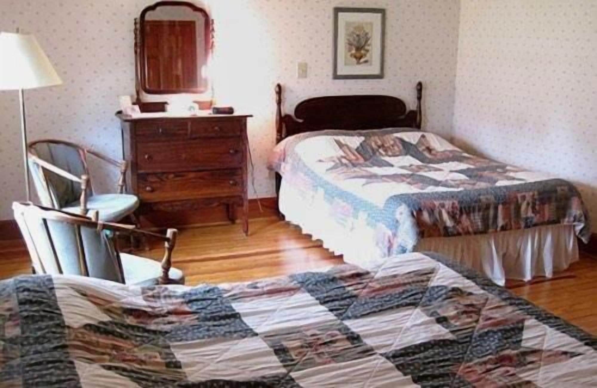 Un dormitorio con cama, cómoda, silla y un cuadro en la pared.