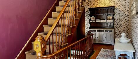 A staircase with wooden balusters and a handrail, leading to a landing with a white cabinet and a small table.