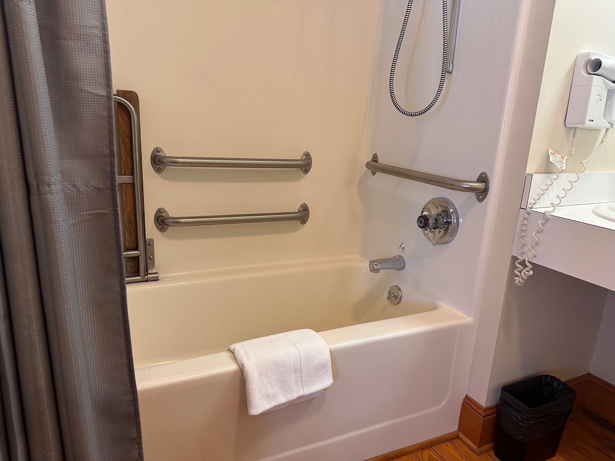 Un baño con bañera, barras de apoyo, cabezal de ducha y un perchero para toallas.