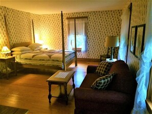 A room with a four-poster bed, a wooden table, a sofa, and a lamp.