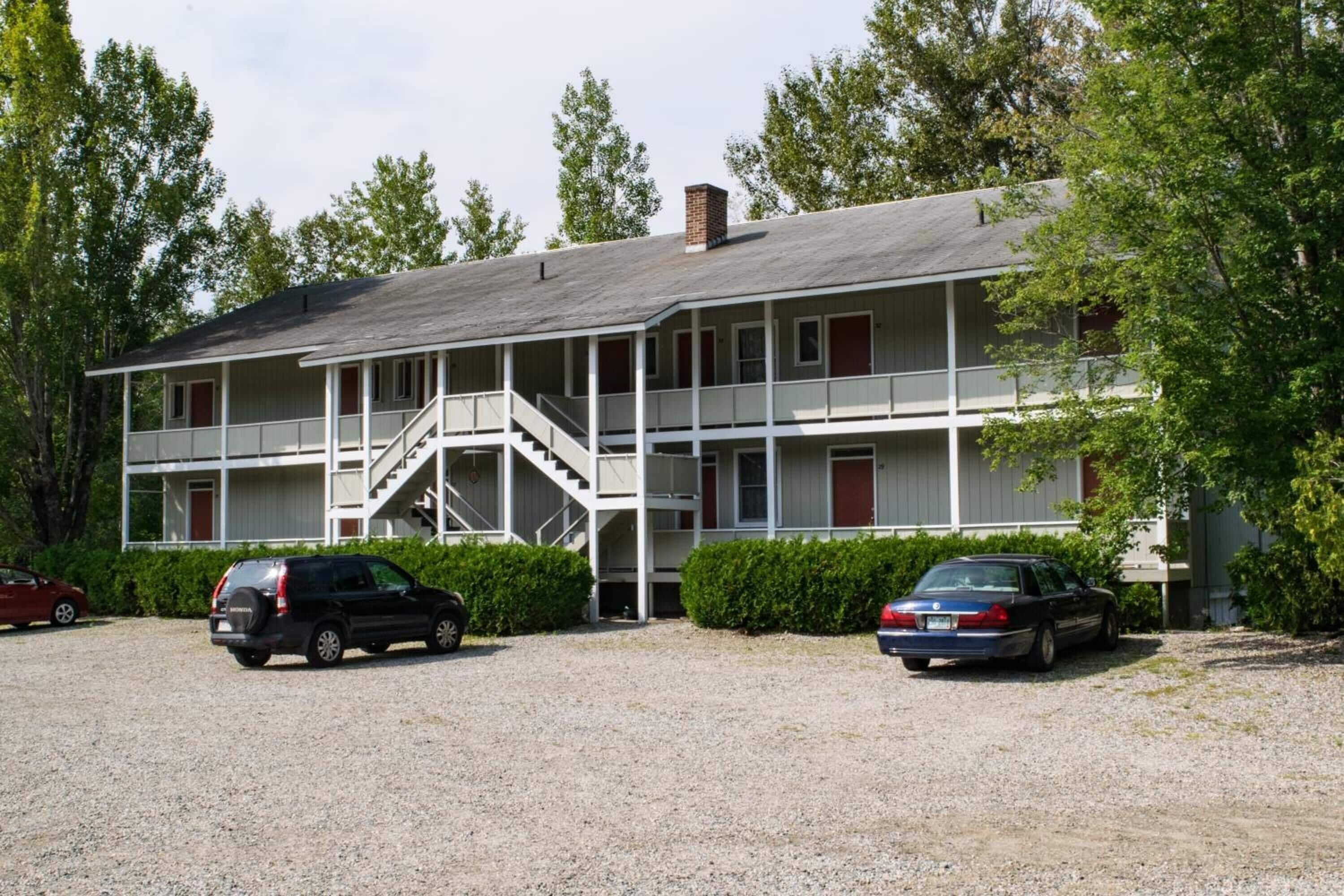 A two-story motel with a central staircase, a covered front porch, and a gravel driveway.