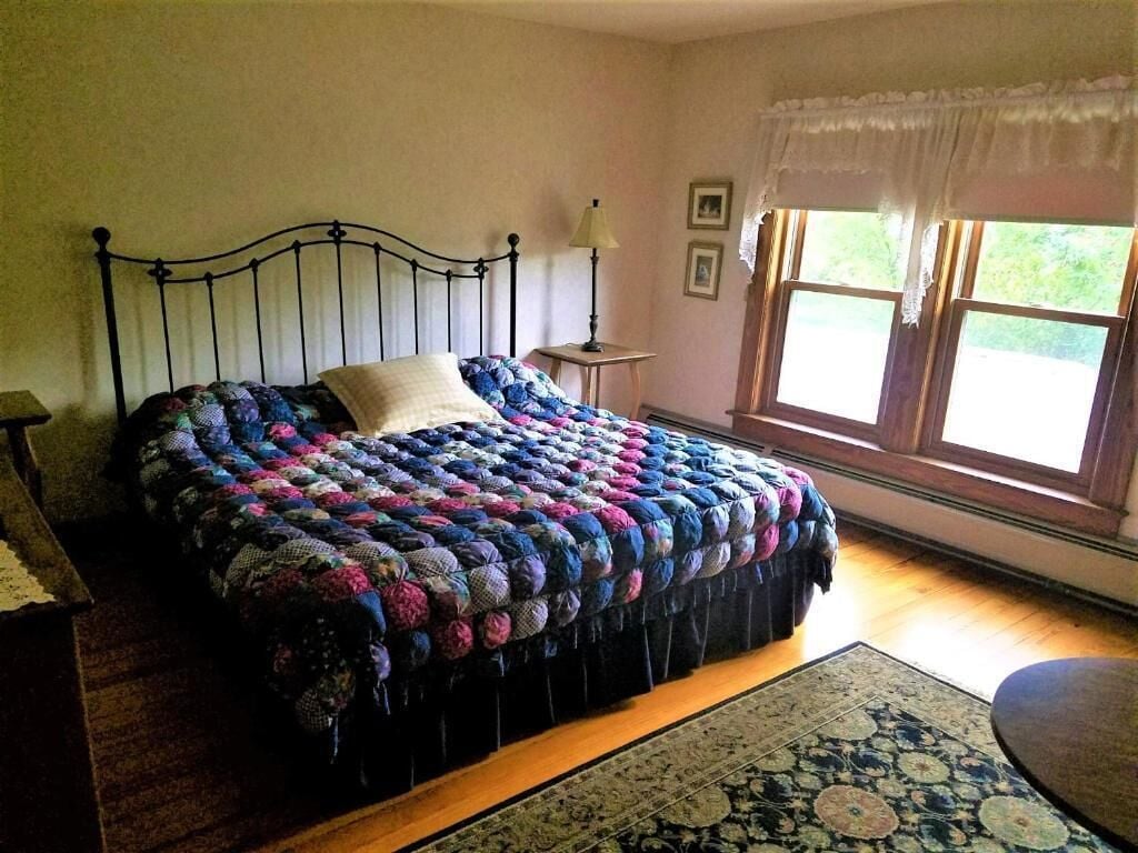 A bedroom with a bed, a nightstand, a lamp, a window with curtains, and a rug.
