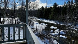 Vista desde un balcón sobre un paisaje nevado con río, árboles y cascabeles de hielo colgando del tejado.