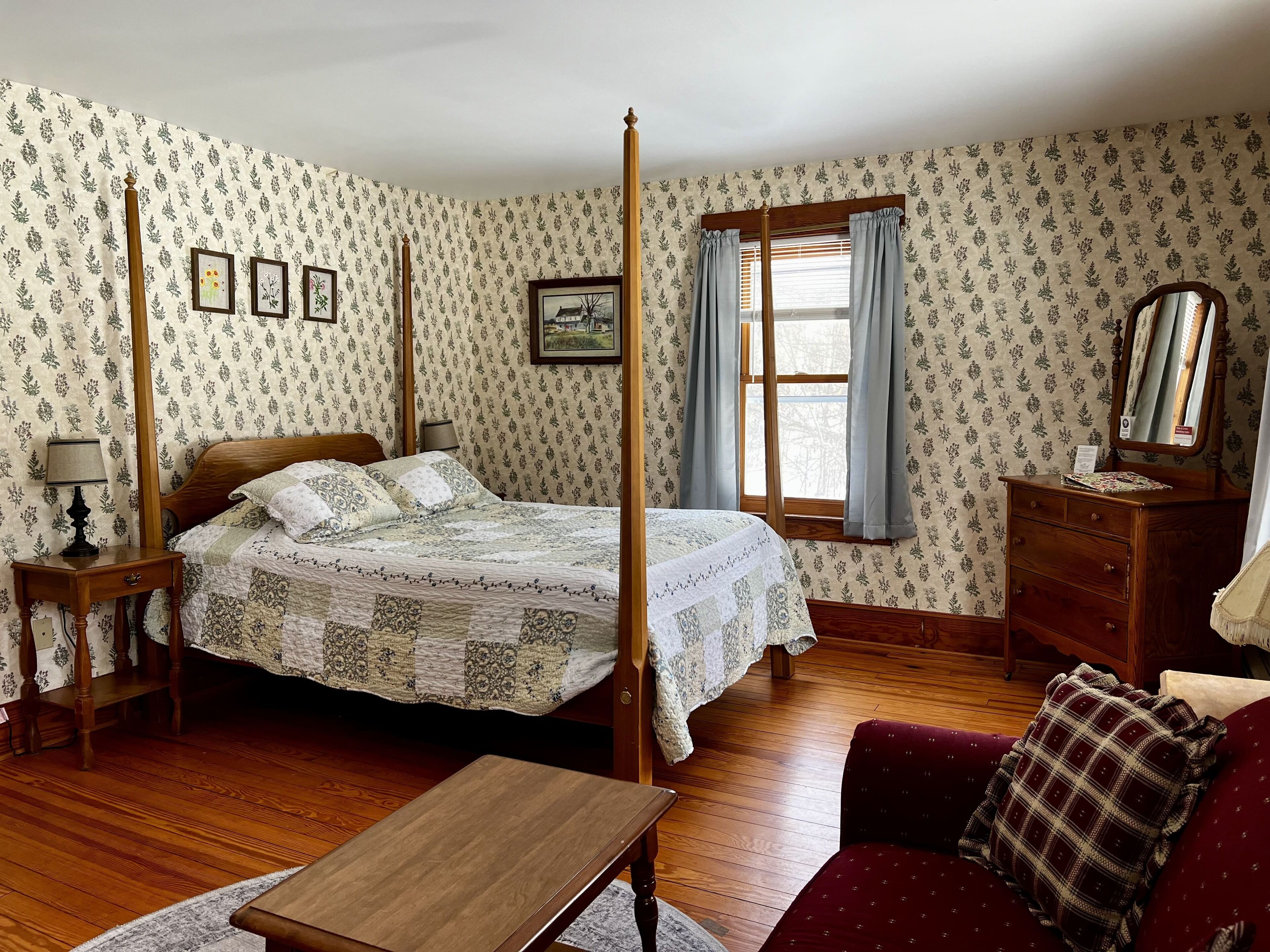 Ein traditionell eingerichtetes Schlafzimmer mit einem Himmelbett, Holzmöbeln und blumigem Wandpapier.