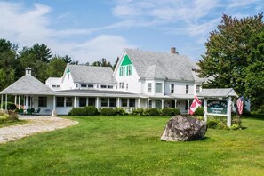 A large, white building with green accents, a covered porch, and a sign indicating it is a bed and breakfast.