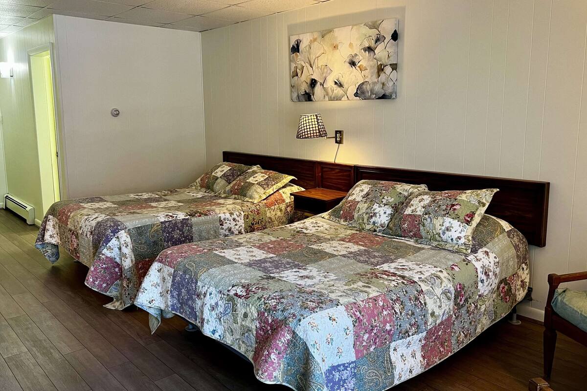 A room with two beds, a wall-mounted lamp, and a floral artwork.
