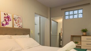 A hotel room with a bed, a green throw blanket, towels, a nightstand, a mirror, and a window. - Flores de Bombinhas (Bombinhas)