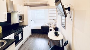 Cocina compacta con electrodomésticos modernos, comedor con mesa y sillas, y una cama litera al fondo.