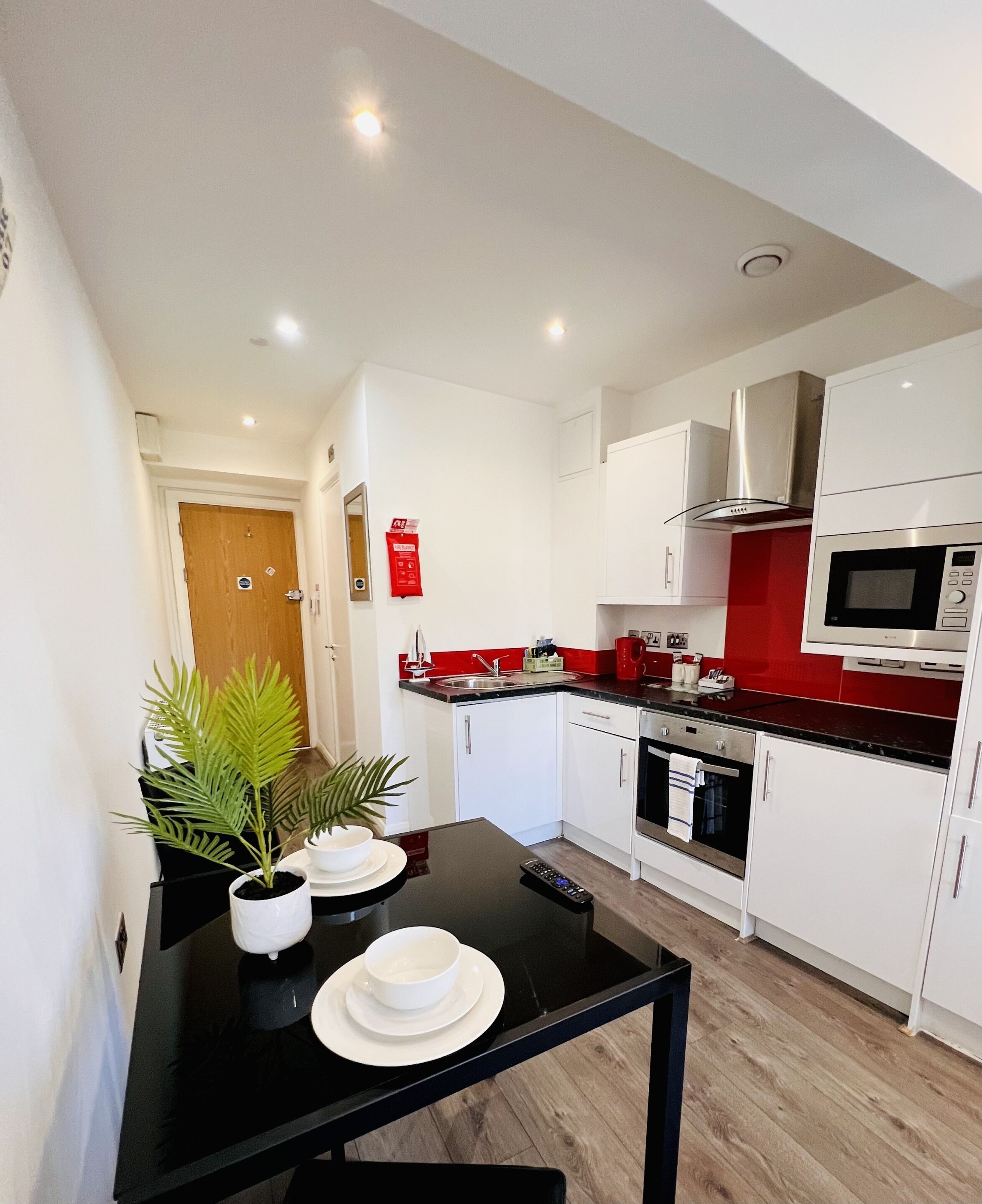 A modern kitchen with white cabinets, a red countertop, and a black dining table with a potted plant.