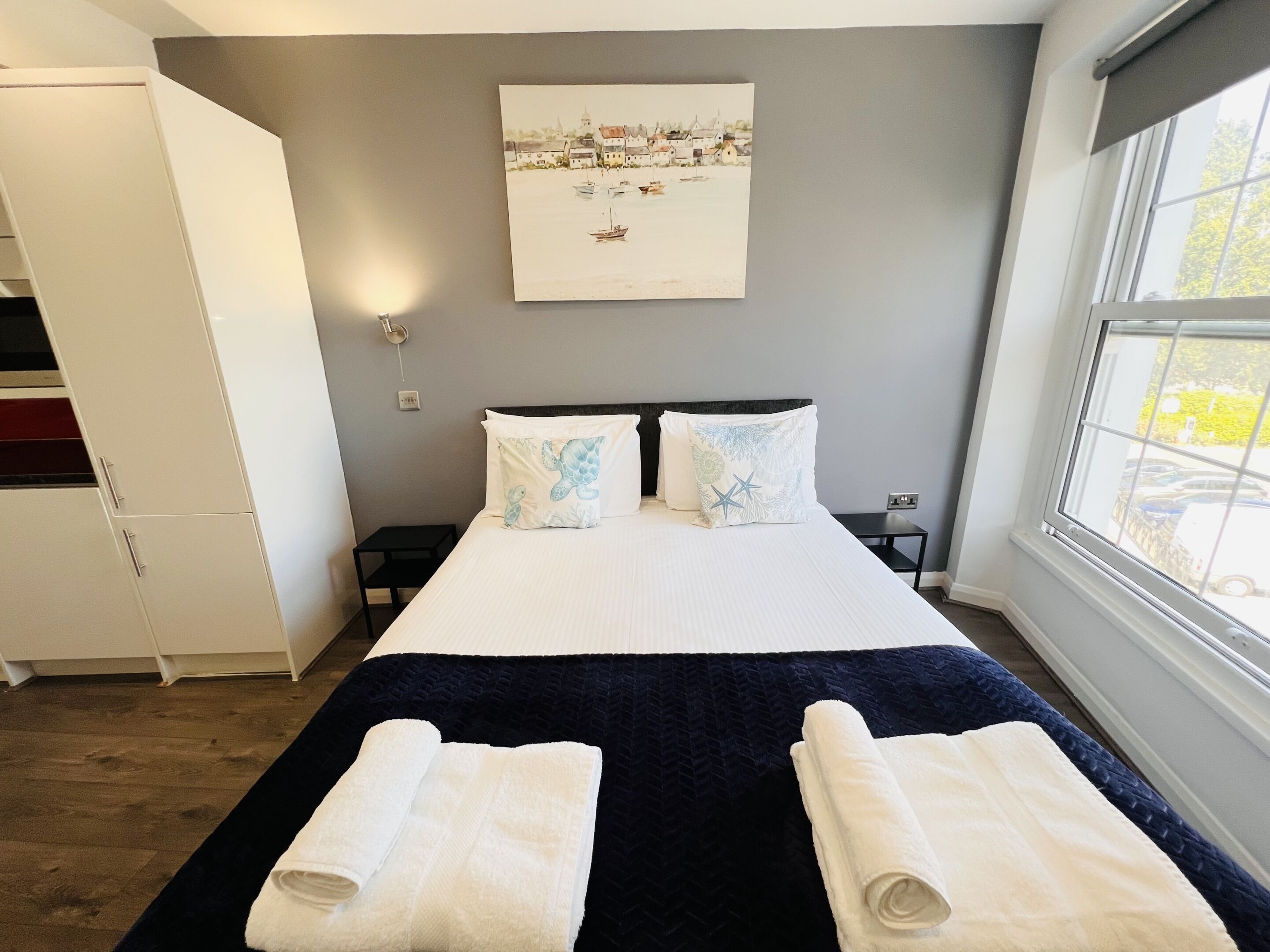 A bedroom with a bed, two nightstands, a painting on the wall, a wardrobe, and a window with a view.
