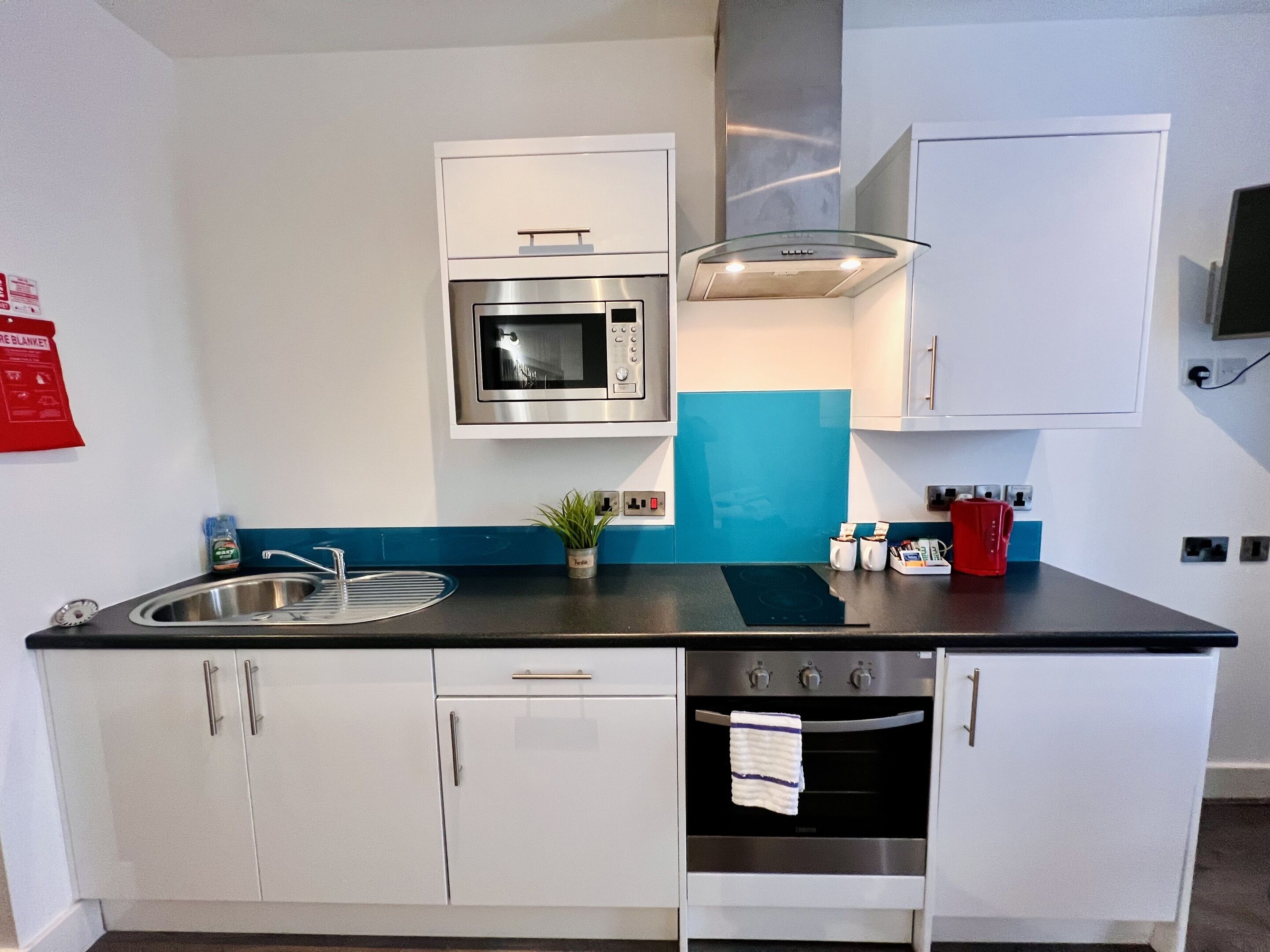 Cocina compacta con armarios blancos, pileta de acero inoxidable, microondas, estufa y un ventanal.