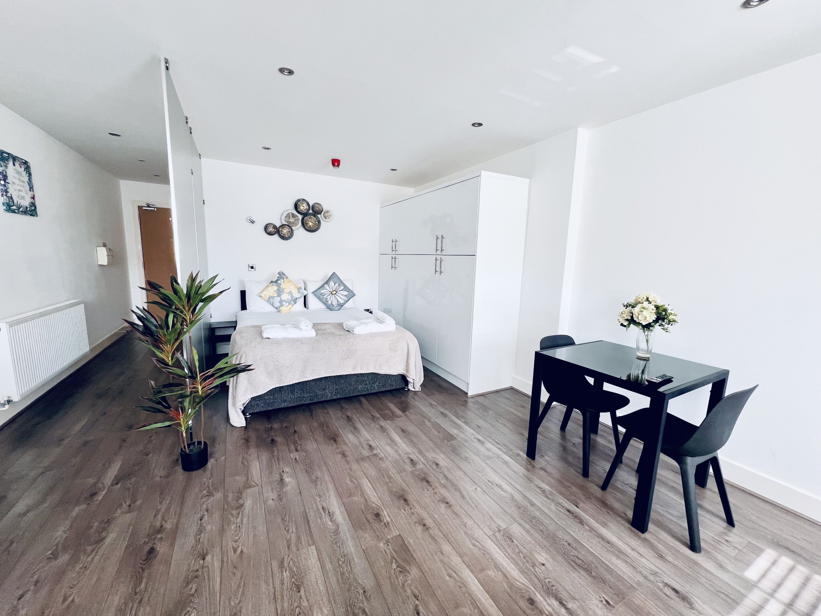 A modern hotel room with a bed, bedside table, and a small dining area with a table and chairs.