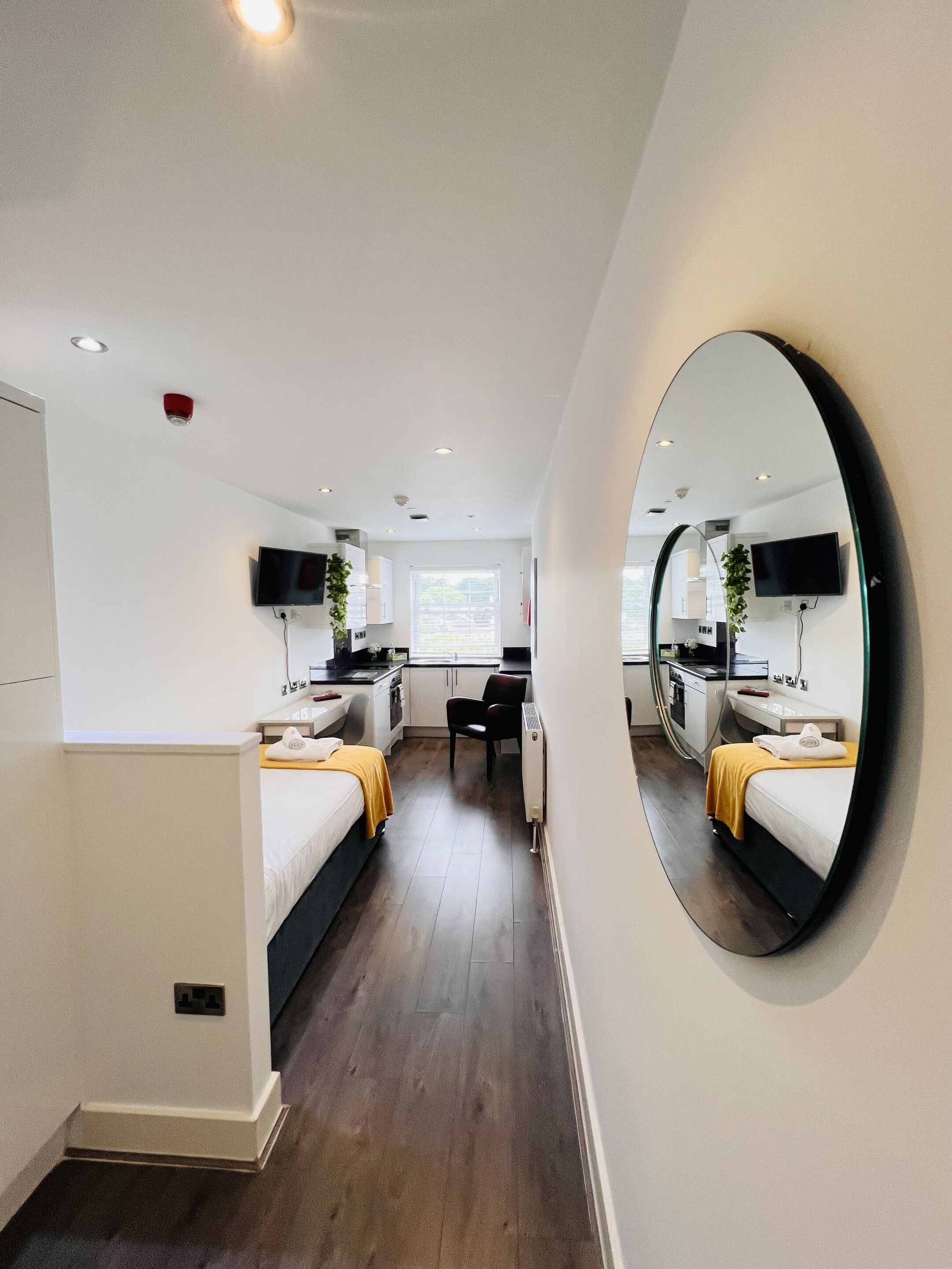 Una habitación de hotel moderna con un espejo grande, una cama, un escritorio y una kitchenette.