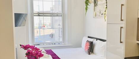 A modern hotel room with a bed, a small table with a vase and bowls, a window with a view of the city, and a white wardrobe.