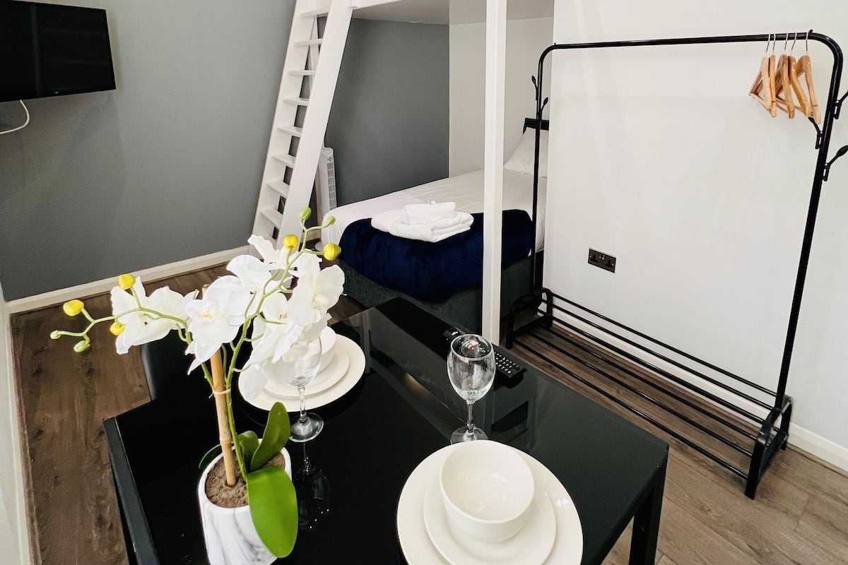 A bunk bed room with a TV mounted on the wall, a table with a vase of flowers, and a black table lamp.
