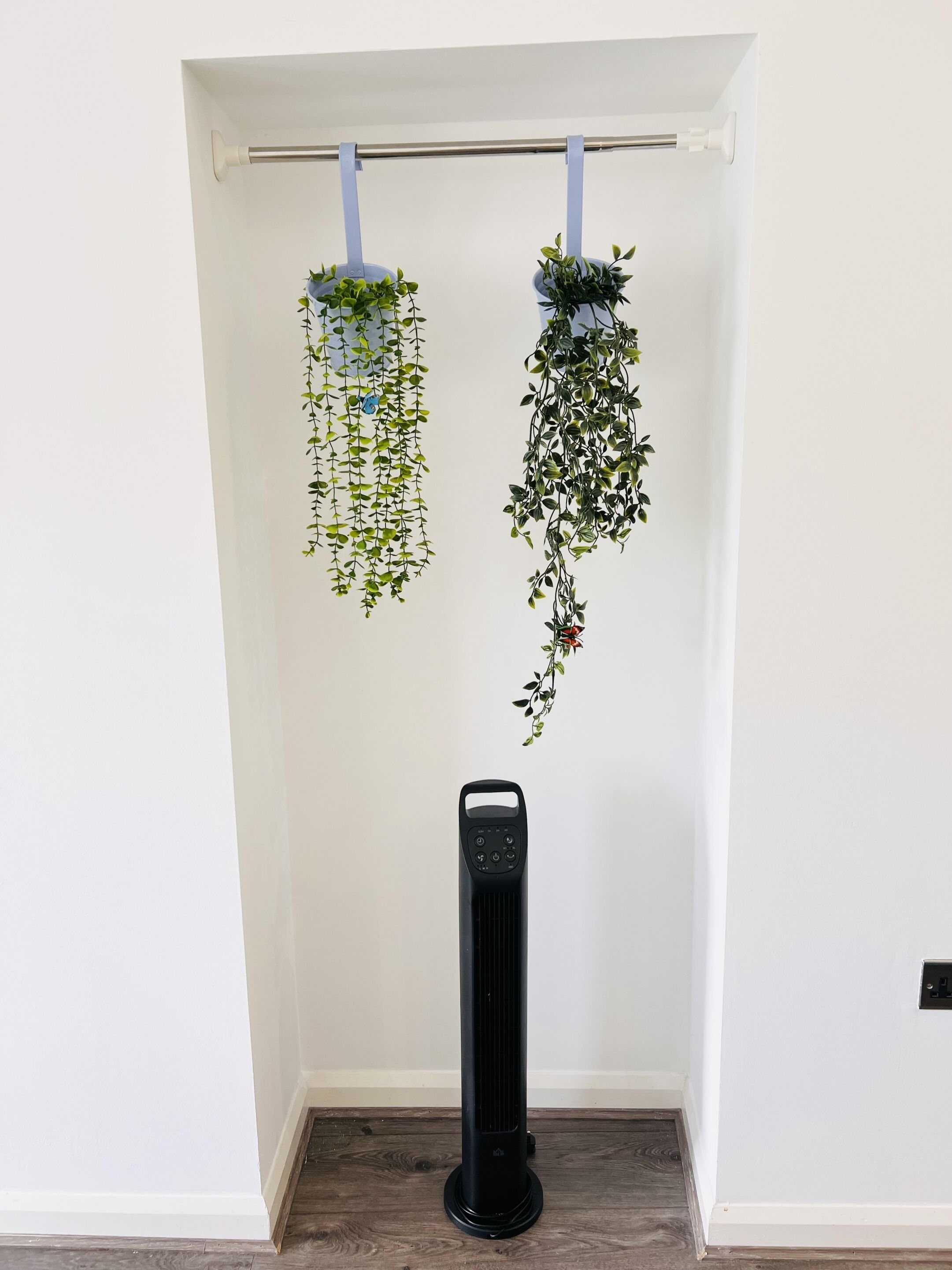 Quarto com parede branca, aquecedor preto e duas plantas penduradas.