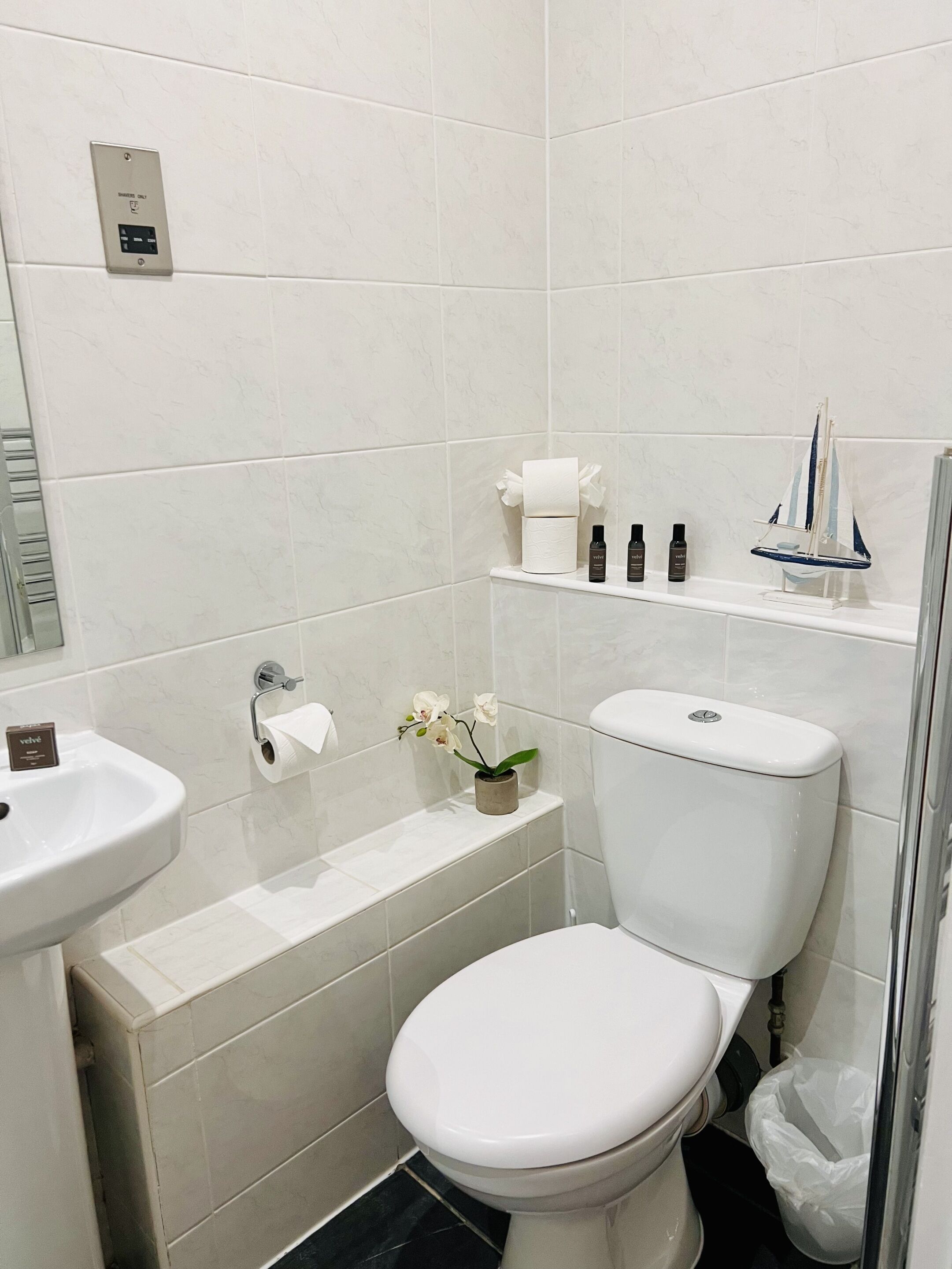 Un baño con inodoro, lavabo y estante con artículos de aseo.