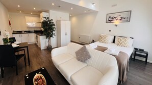 Un apartamento moderno con sala de estar, una mesa de comedor con una planta, cocina y un dormitorio con cama y un cuadro.