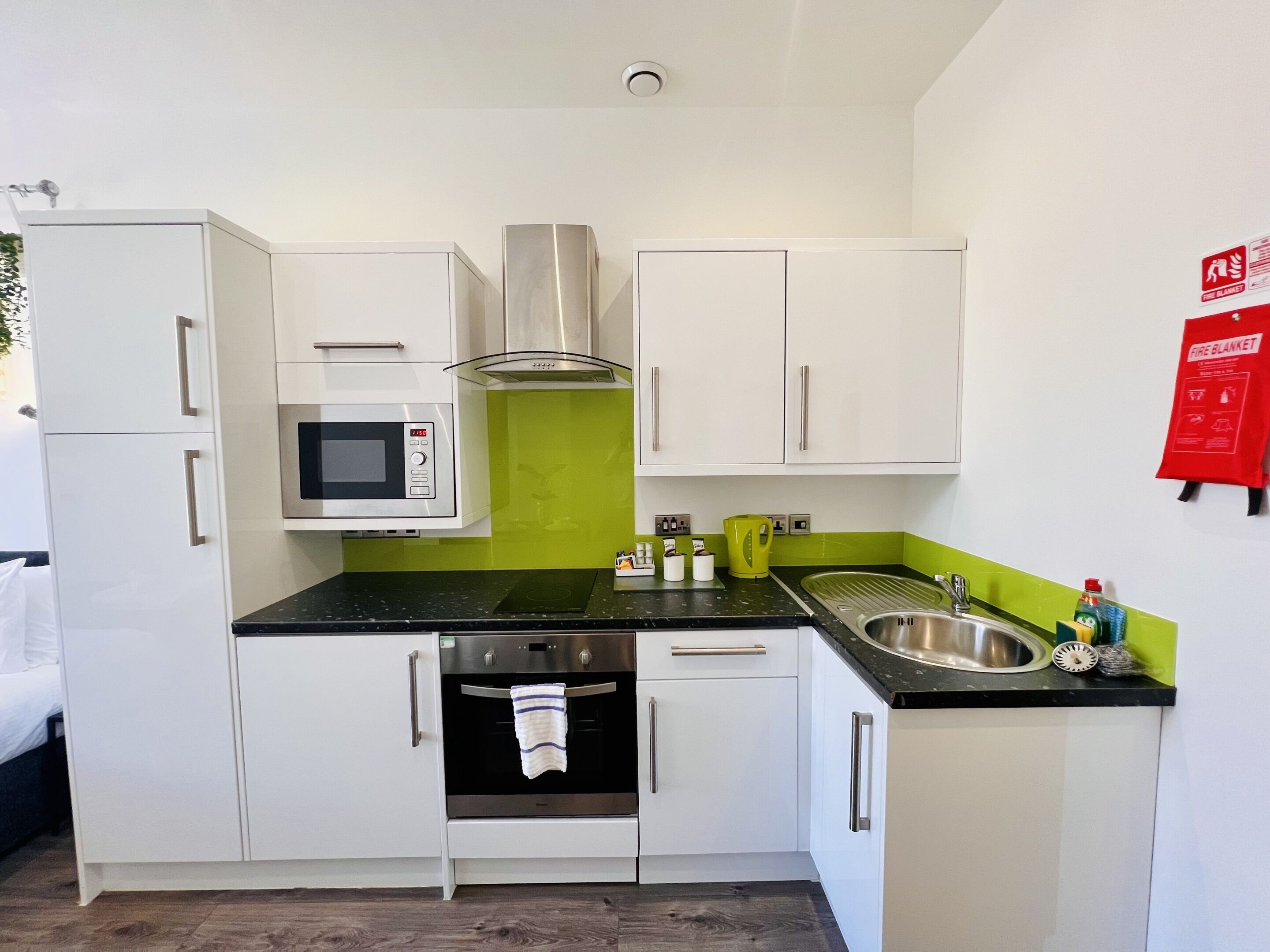 A compact kitchen with white cabinets, a microwave, an oven, a sink, and a green backsplash.