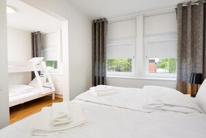 A hotel room with a bunk bed, a single bed, and a window with curtains.