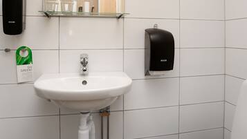 A bathroom with a white sink, a mirror, a toilet, and two soap dispensers.