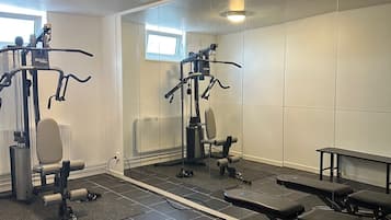 Een sportschool met fitnessapparatuur, een bank en een spiegelwand.