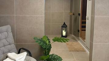 A modern bathroom with a grey cushioned chair, a potted plant, and a lantern.