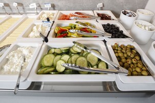 A buffet with various food options including cream cheese, cucumbers, olives, and vegetables.