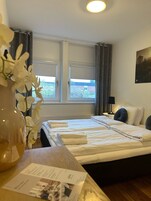 A hotel room with two beds, a window with curtains, a vase of flowers, and a painting on the wall.