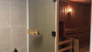 Un cuarto de sauna con bancos de madera, una puerta de cristal y un aplique en la pared.