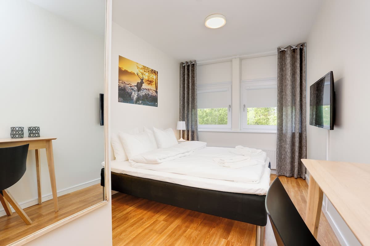 Une chambre à coucher avec un lit, un bureau, une chaise, un téléviseur et une fenêtre avec des rideaux.