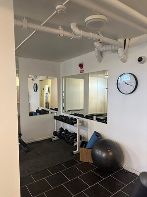 A gym with exercise equipment, a clock, and mirrors.