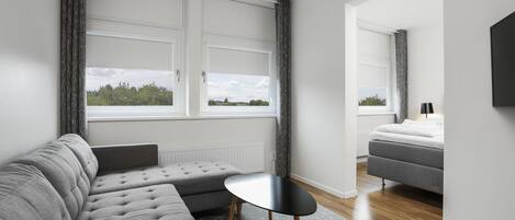 Un salón moderno con un sofá gris, una mesita redonda y una cama en la habitación contigua.