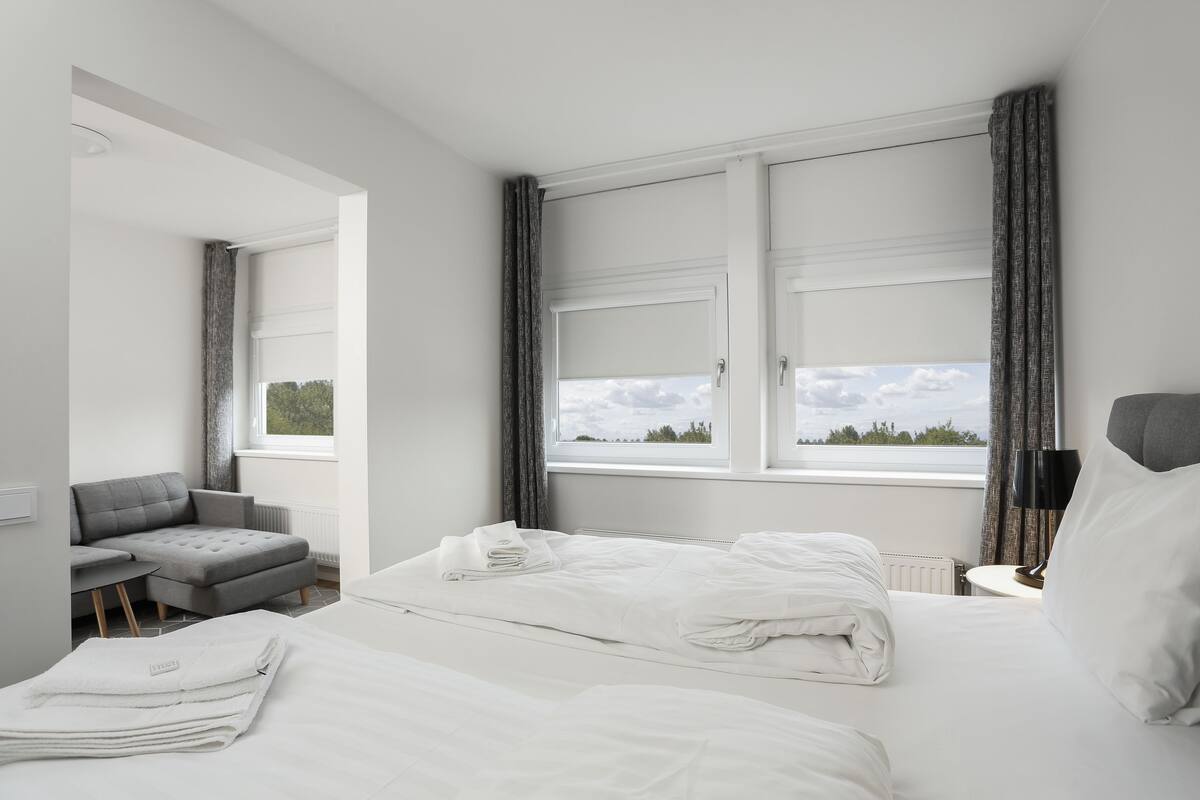 Une chambre d’hôtel avec un lit, un canapé gris et une vue sur l’extérieur.
