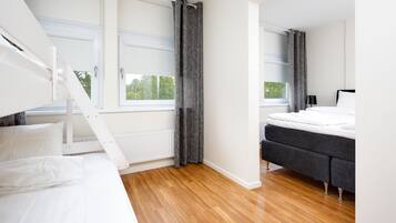 A modern bedroom with a bunk bed, a grey sofa bed, and a large window with curtains.