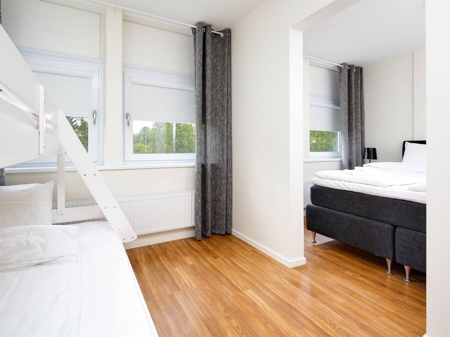 A modern bedroom with a bunk bed, a grey sofa bed, and a large window with curtains.