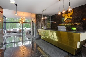 A hotel reception area with a modern design, featuring a gold reception desk, a large chandelier, and a logo on the wall.