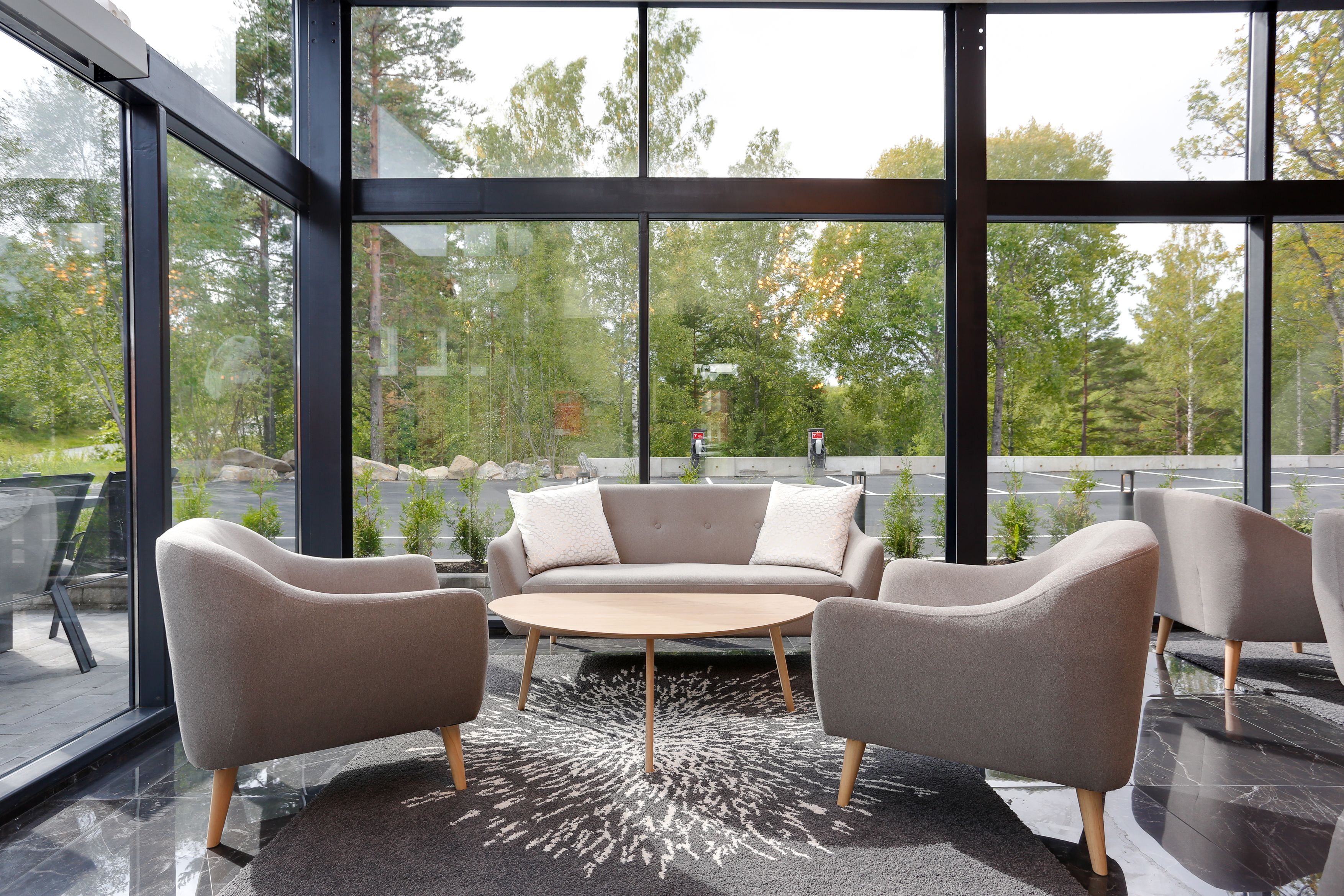 Un interior moderno con un sofá y dos sillones frente a un ventanal con vistas a un bosque.