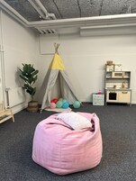 Un cuarto de juegos infantil con un sillón de tela rosa, una pequeña tienda de campaña, globos y un juego de cocina.