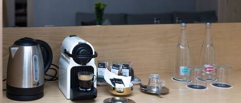 A kitchenette with a coffee maker, kettle, and glass bottles on the counter.