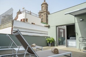 Une terrasse sur le toit, avec des chaises longues, un pot de fleurs et une vue sur une tour historique.
